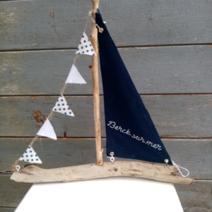 Bateau en bois flotté avec une voile bleu marine et une inscription berck sur mer en broderie fait main ainsi qu'une guirlande de petits fanions tissus blanc et petits pois bleus