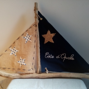 Bateau en bois flotté avec deux voiles. Une voile en tissus bleu marine avec inscription " Côte d'Opale' en broderie rose clair et une autre voile en toile de jute avec des étoiles de tissus blanc à petits pois blanc.