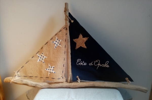 Bateau en bois flotté avec deux voiles. Une voile en tissus bleu marine avec inscription " Côte d'Opale' en broderie rose clair et une autre voile en toile de jute avec des étoiles de tissus blanc à petits pois blanc.