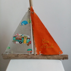 Bateau en bois flotté avec deux voiles. Une voile couleur orange et une inscription " Côte d'Opale" en broderie jaune et une autre voile avec des imprimés combi.