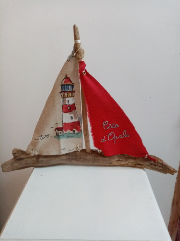 Bateau en bois flotté avec deux voiles. Une voile rouge et une inscription " Côte d'Opale" en broderie bleu clair et une autre voile avec un imprime d'un phare.