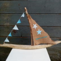 Bateau en bois flotté avec une voile en toile de jute et inscription " Berck sur mer" en broderie bleu clair et une banderole de tissus bleu ciel à petits pois blanc et tissus rayé .