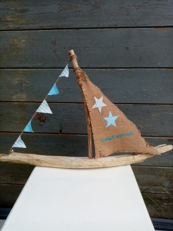 Bateau en bois flotté avec une voile en toile de jute et inscription " Berck sur mer" en broderie bleu clair et une banderole de tissus bleu ciel à petits pois blanc et tissus rayé .