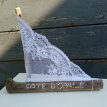 Petit bateau en bois flotté avec une voile en véritable dentelle de Calais. Une inscription " Côte d'Opale" faite avec un outil de pointage d'art et peinture blanche