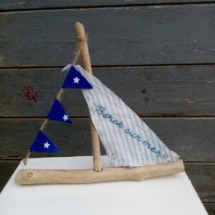 Petit bateau en bois flotté avec une voile blanche et rayure gris clair avec une inscription " berck sur mer" en broderie bleu et une banderole avec tissus bleu marine