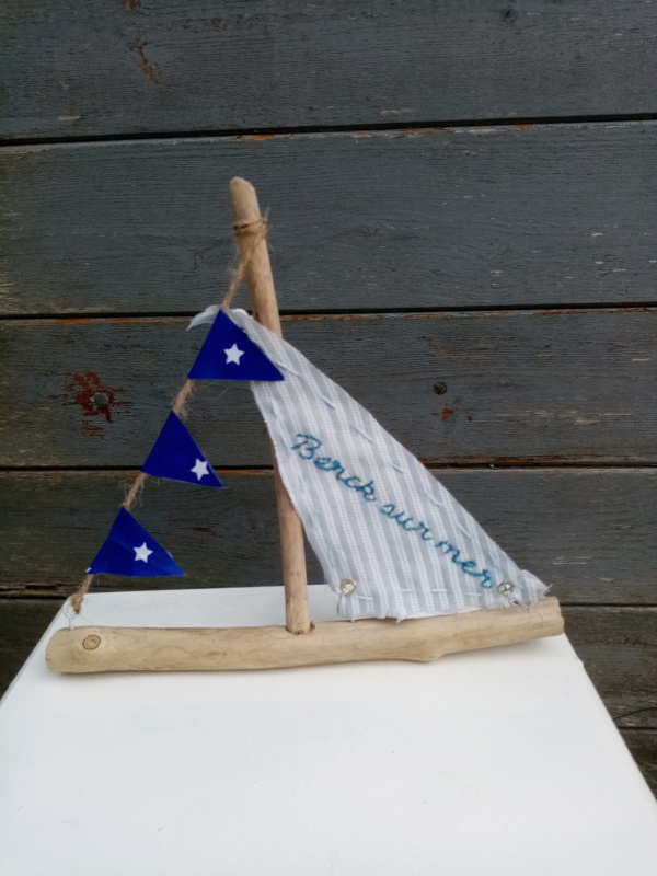 Petit bateau en bois flotté avec une voile blanche et rayure gris clair avec une inscription " berck sur mer" en broderie bleu et une banderole avec tissus bleu marine