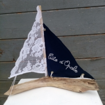 petit bateau en bois flotté avec deux voiles. Une voile en tissus bleu marine avec inscription " Côte d'opale" en broderie blanche et une autre voile en véritable dentelle de Calais.