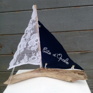 petit bateau en bois flotté avec deux voiles. Une voile en tissus bleu marine avec inscription " Côte d'opale" en broderie blanche et une autre voile en véritable dentelle de Calais.