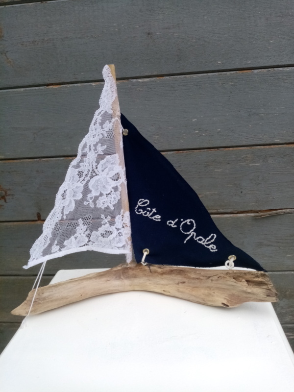 petit bateau en bois flotté avec deux voiles. Une voile en tissus bleu marine avec inscription " Côte d'opale" en broderie blanche et une autre voile en véritable dentelle de Calais.